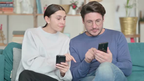 Hispanic Couple Using Smartphone and Talking While Sitting