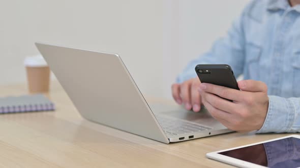 Man Using Laptop with Smartphone