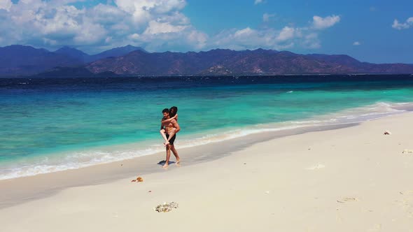 Man holding on his shoulders girlfriend, walking along white sand of exotic beach, watching beautifu