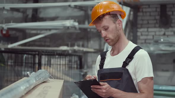 Factory Man Is Checking Cardboard Box and Looking at the Clipboard in Warehouse