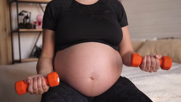 Pregnant Woman Goes in for Sports with Dumbbells Sitting at Home on the Bed