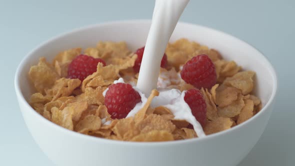 Corn flakes with raspberry in a bowl pouring with milk. Slow Motion.