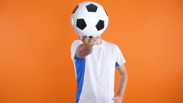 Football Fan In White Blue Shirt Standing Still and Holding Ball in Front of His Face with One Hand