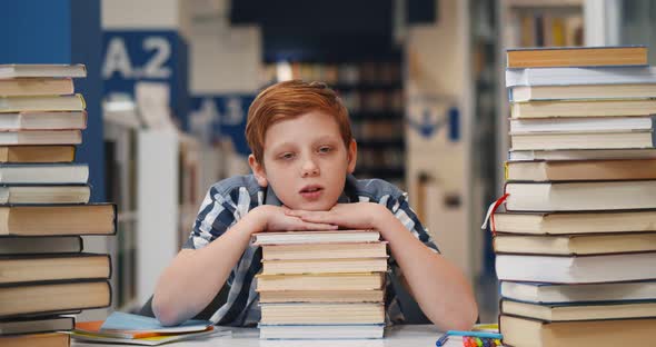 Tired Teen Student Sleeping on Stack of Books on Desk in Library