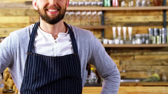 Smiling waiter standing with hands on hip at counter