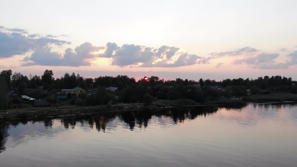 Sunset at river town, small houses seen down, aerial camera move up