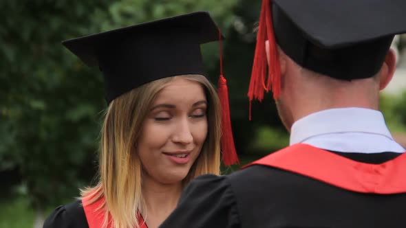 Beautiful Woman in Academic Dress Talking to Graduating Boyfriend After Ceremony