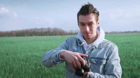 Young Male Photographer Taking Photo on Professional Photocamera Standing at Beautiful Green Field