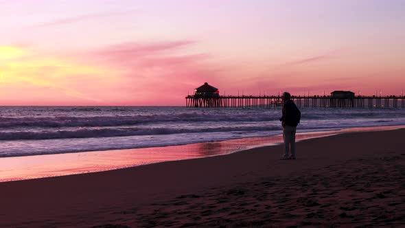 A man takes a picture of the beach during a gorgeous yellow, orange, pink and blue sunset with the H