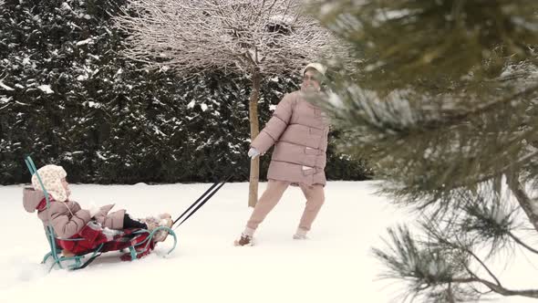 Young Happy Mother and Her Daughter Enjoying a Sledge Ride in a Beautiful Snowy Backyard