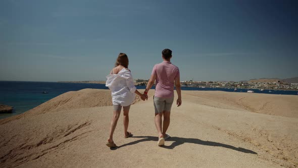 a Man in a Pink Tshirt and a Woman with Long Hair in a White Shirt Walk Away Along a Deserted Sandy