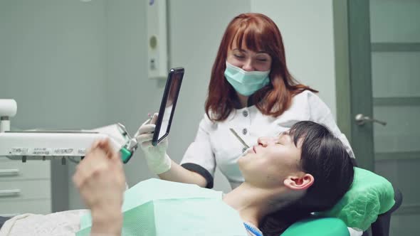 A dentist gives brunette a mirror for inspecting the result after the teeth whitening procedure