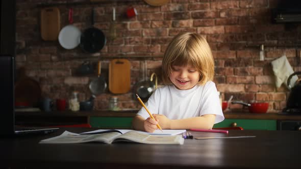 Kid in White Tshirt Sticking Out Tongue Smiling Writing Letters in School Notebook