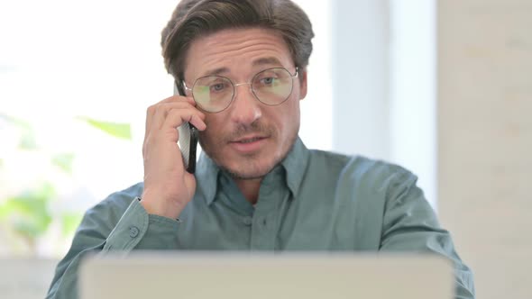 Middle Aged Man with Laptop Talking on Phone