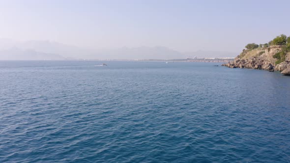 Landscape with Yacht Floating on Sea with Rocky Seashore in the Background