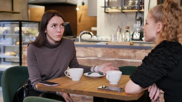 Young Blonde and Brunette at a Table in a Restaurant Talking and Drinking Tea