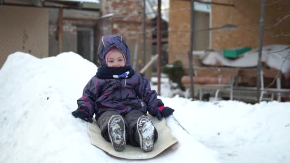 A Child Rolls on a Snow Slide. Winter Fun on the Street. In the Cold Winter, the Child Is Dressed