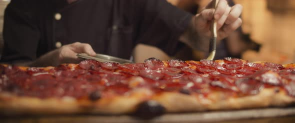 Italian chef spreading olive oil with brush over traditional pepperoni al taglio pizza. Close up