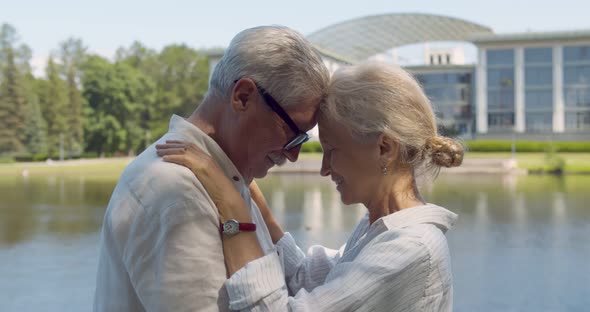 Side View Portrait of Senior Couple Hugging Outdoors Near Lake