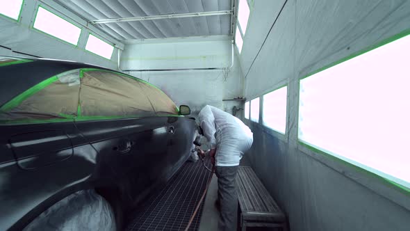 Car body painter spraying car in paint booth