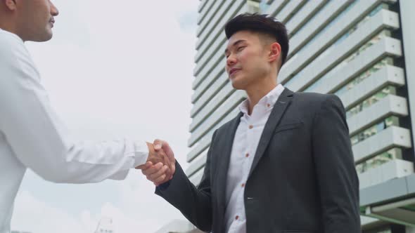 Asian businessmen making handshake greeting with co worker in the city building in background.