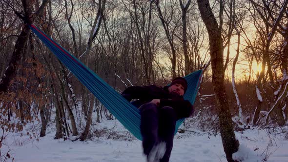 man lying in hammock under the trees in the winter forest