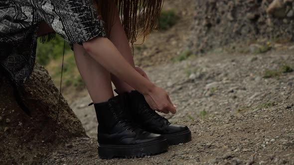 A Girl in a Gray Cape Sits on a Stone and Ties Her Shoelaces