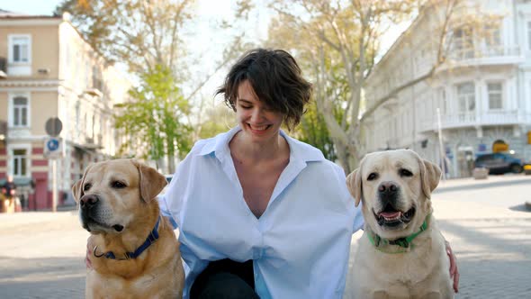 Portrait of Young Stylish Hipster Girl Petting Two Retriever Dogs Outdoors in City Center