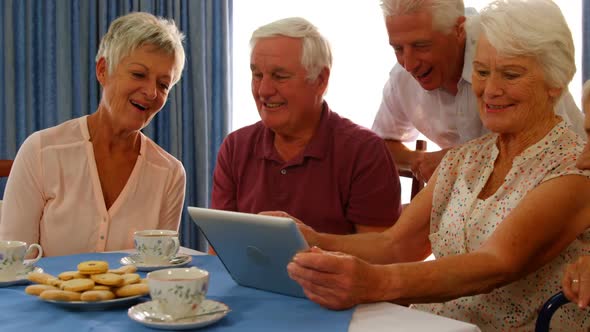 Group of happy senior friends looking at digital tablet and laughing