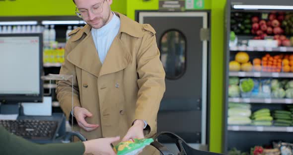 Handsome Young Man Standing at Cash Register and Puts Groceries at the Checkout