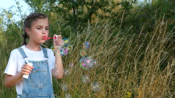 Happy Little Girl in the Park Blows Soap Bubbles