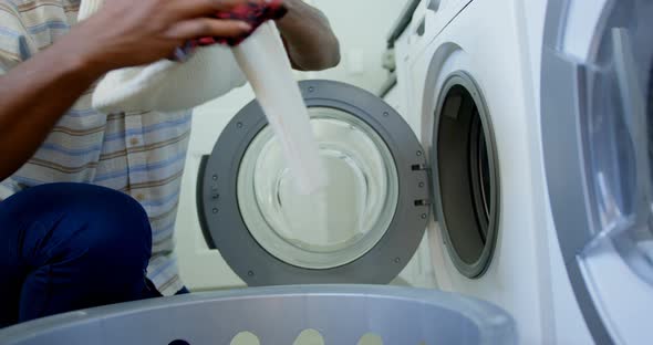 Side view of mid adult black man washing clothes in washing machine at comfortable home 4k