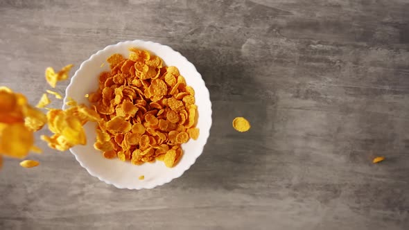 Dry Sweet Breakfast Consisting of Yellow Cornflakes Flying in Slowmo From Above Into a White Plate