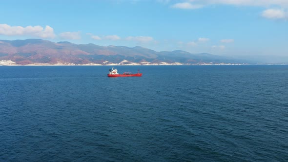 Aerial View of Red Color Cargo Ship Floating at Sea Port, Mountain on Background