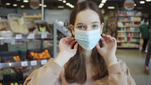 A Beautiful Girl Puts on a Medical Protective Mask in the Supermarket