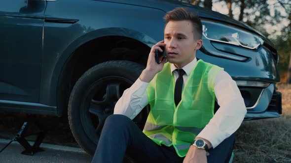 Young Man is Using the Phone in Asking for Help When His Car is Broken Man in a Green Safety Vest