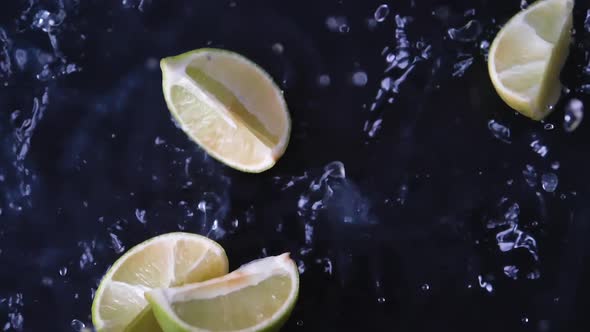 Fresh slices of green lime fruit dropping into water with splashes in slowmotion.