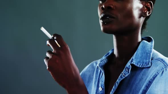 Androgynous man posing with cigarette against dark background