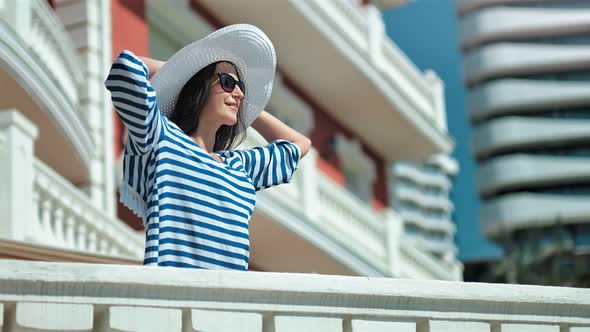 Glamour Young Woman Having Good Time Outdoor Raising Hands and Holding Hat on Her Head Enjoying Sun