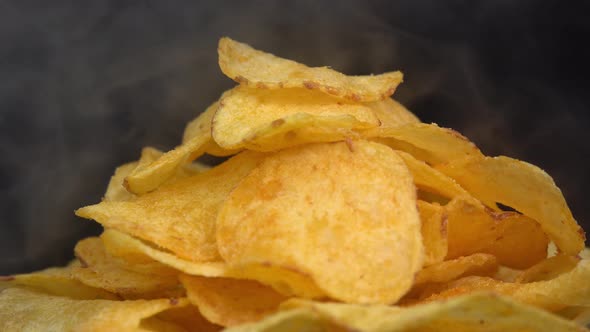 Craft crispy hot potato chips with smoke rotating on black background close up. Golden fried
