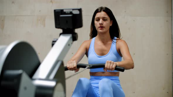 Sporty Young Woman Training on Rowing Machine in Gym