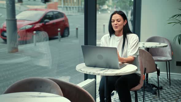 A beautiful woman works on a laptop, leads a zoom call in a cafe. Freelancer, businessman.