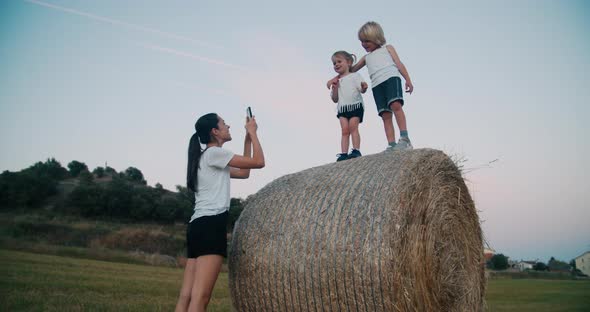 Happy Woman Make a Photo of Her Little Cute Blondes Kids on Haystack in a Field