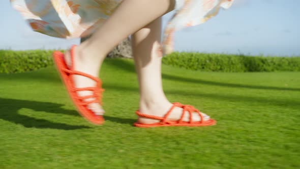 Slow Motion Woman Feet Walking in Bright Orange Red Woven Sandals By Green Lawn