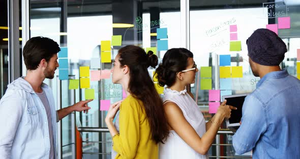 Executives discussing over sticky notes on glass wall