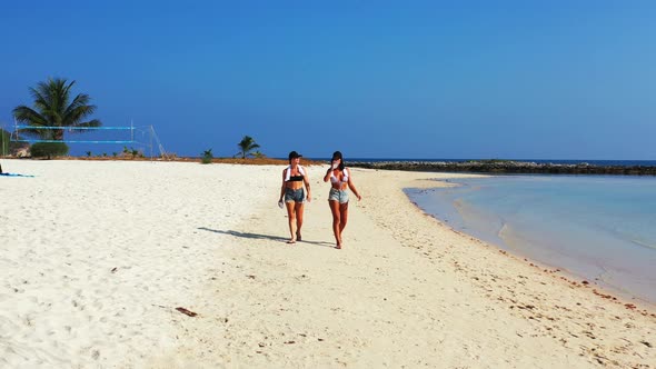 Young smiling girls on photoshoot in the sun at the beach on paradise white sand and blue background