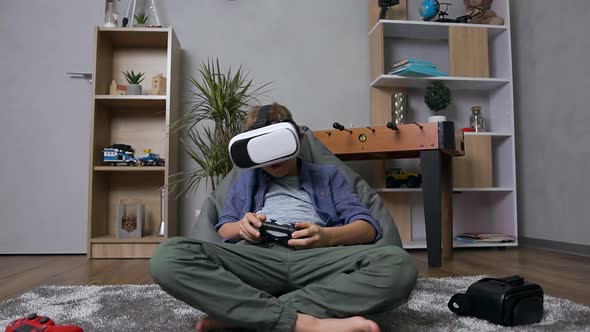 Teen Boy which Sitting on the Bean Bag Sofa and Having Fun at the Playing Video Game Using Joystick 