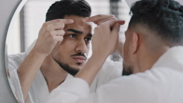 Unhappy Arabian Indian Arab Bearded Man Looking in Bathroom Mirror Feeling Worried About Facial Skin