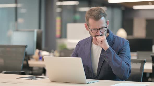 Middle Aged Businessman Coughing While Using Laptop in Office