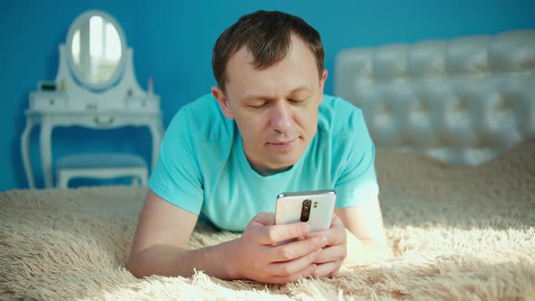 Young man lies in the bedroom on the bed with a mobile phone in his hands